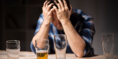 man sitting at a table with his head in his hands struggling with alcohol addiction