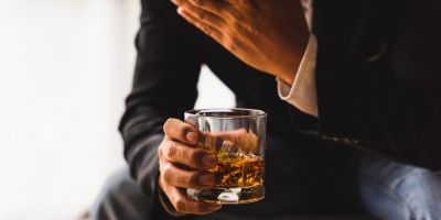 man holding a glass of whiskey showing signs of someone who needs alcohol detox