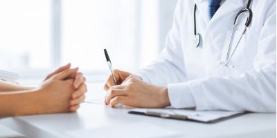 doctor talking to patient with pen in hand at desk. patient holding hands