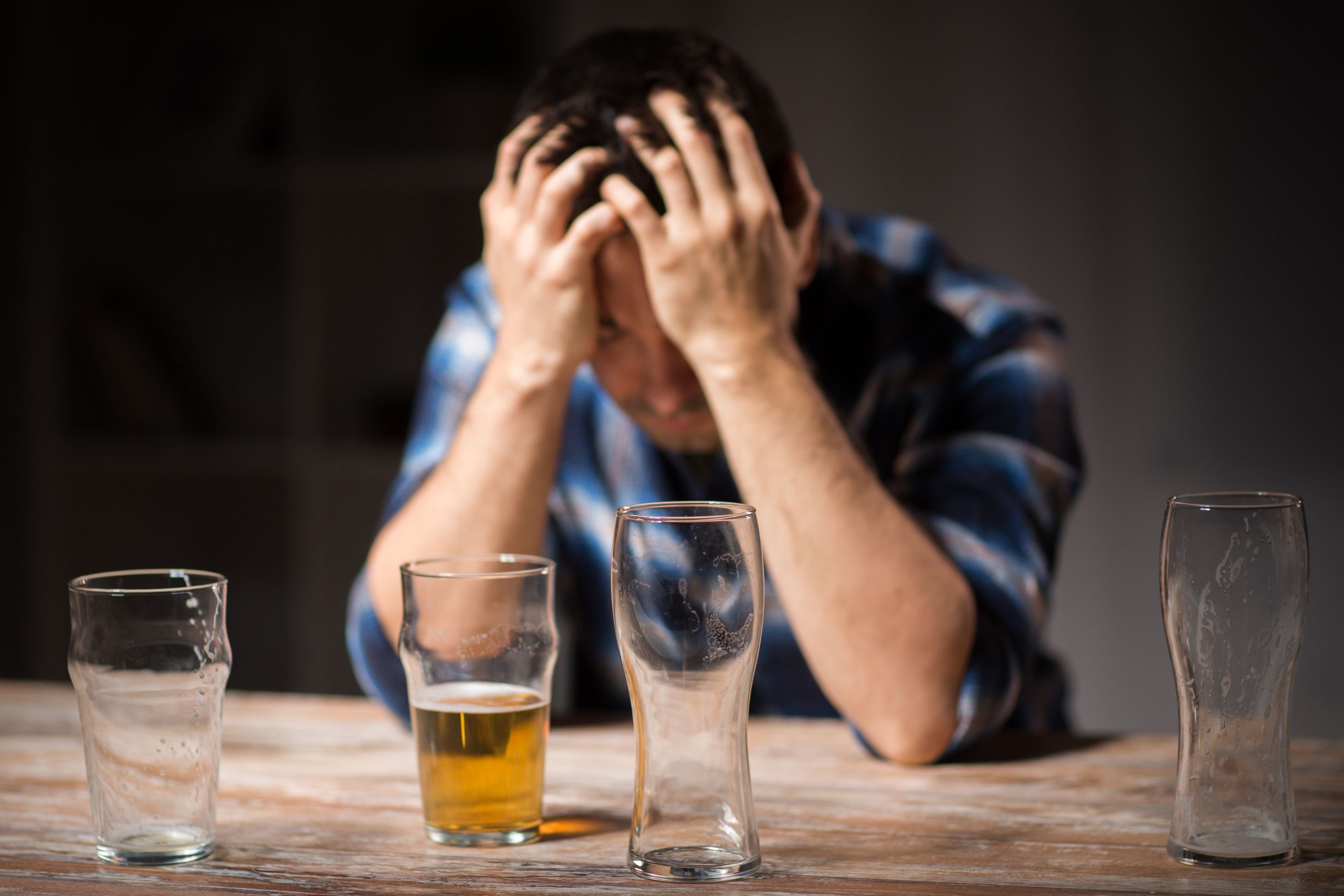 man sitting at a table with his head in his hands struggling with alcohol addiction